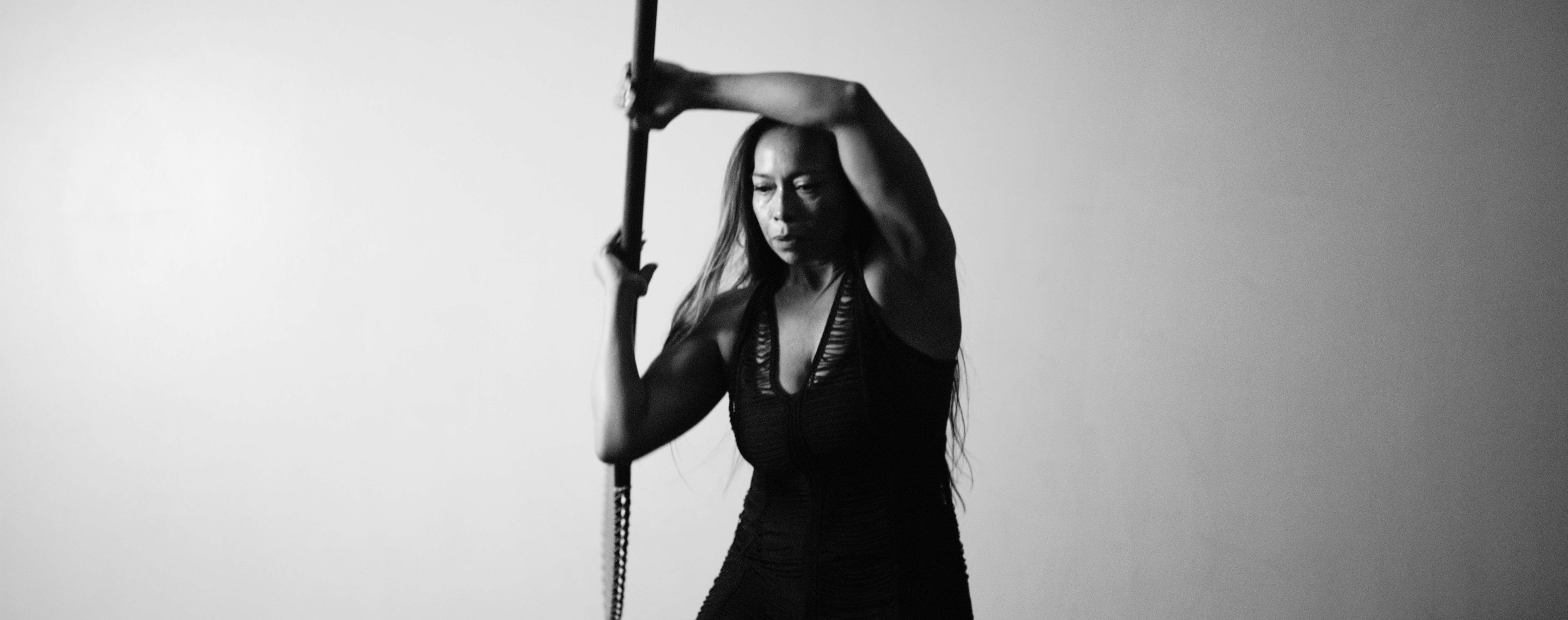 Black-and-white photo of Dr. Michelle Manu, holding a sword vertically with one hand above her head and the other gripping the blade’s hilt, standing in a poised martial arts stance.